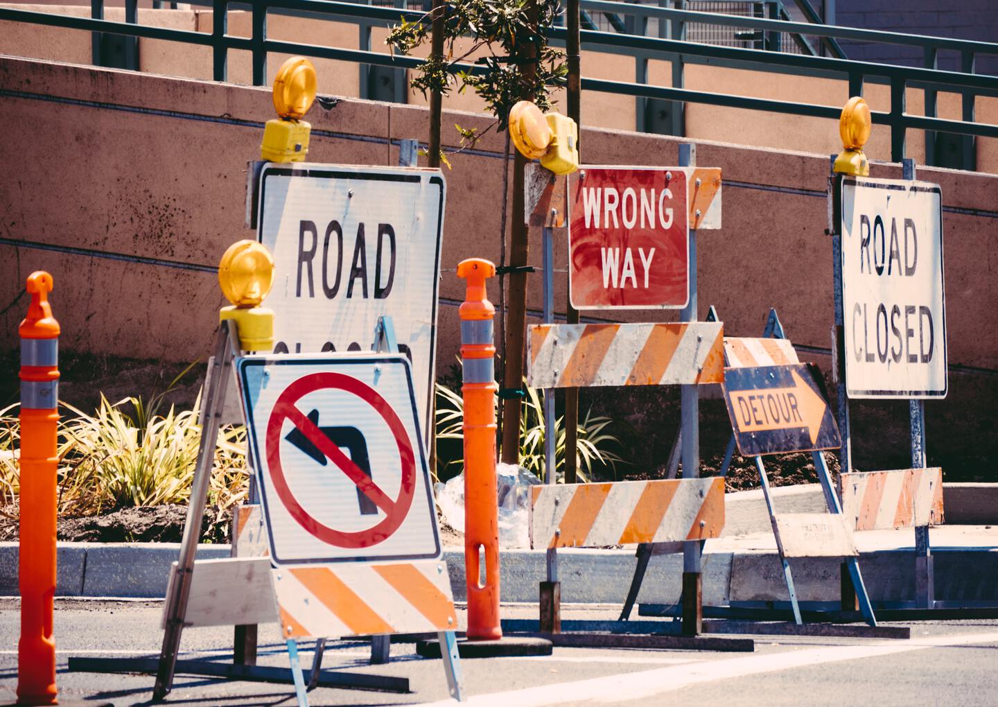 a closed off road with multiple signs reading road closed, wrong way, and detour